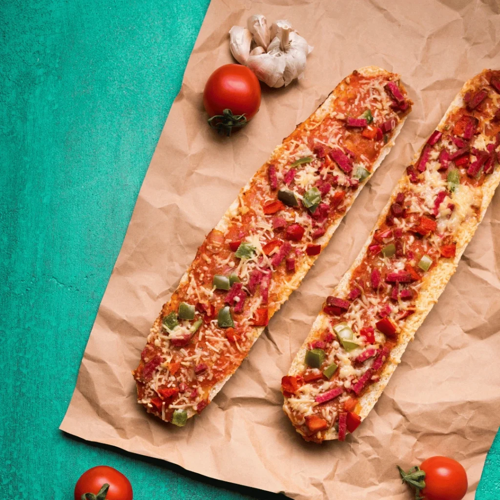 How to Make Perfect Pizza Sticks in 5 Simple Steps 2 Toasted French bread pizza topped with melted cheese, diced bell peppers, tomatoes, and herbs on parchment paper.