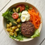 Deconstructed burger bowl recipe with ground beef, lettuce, tomatoes, pickles, cheese, and sauce in a bowl.